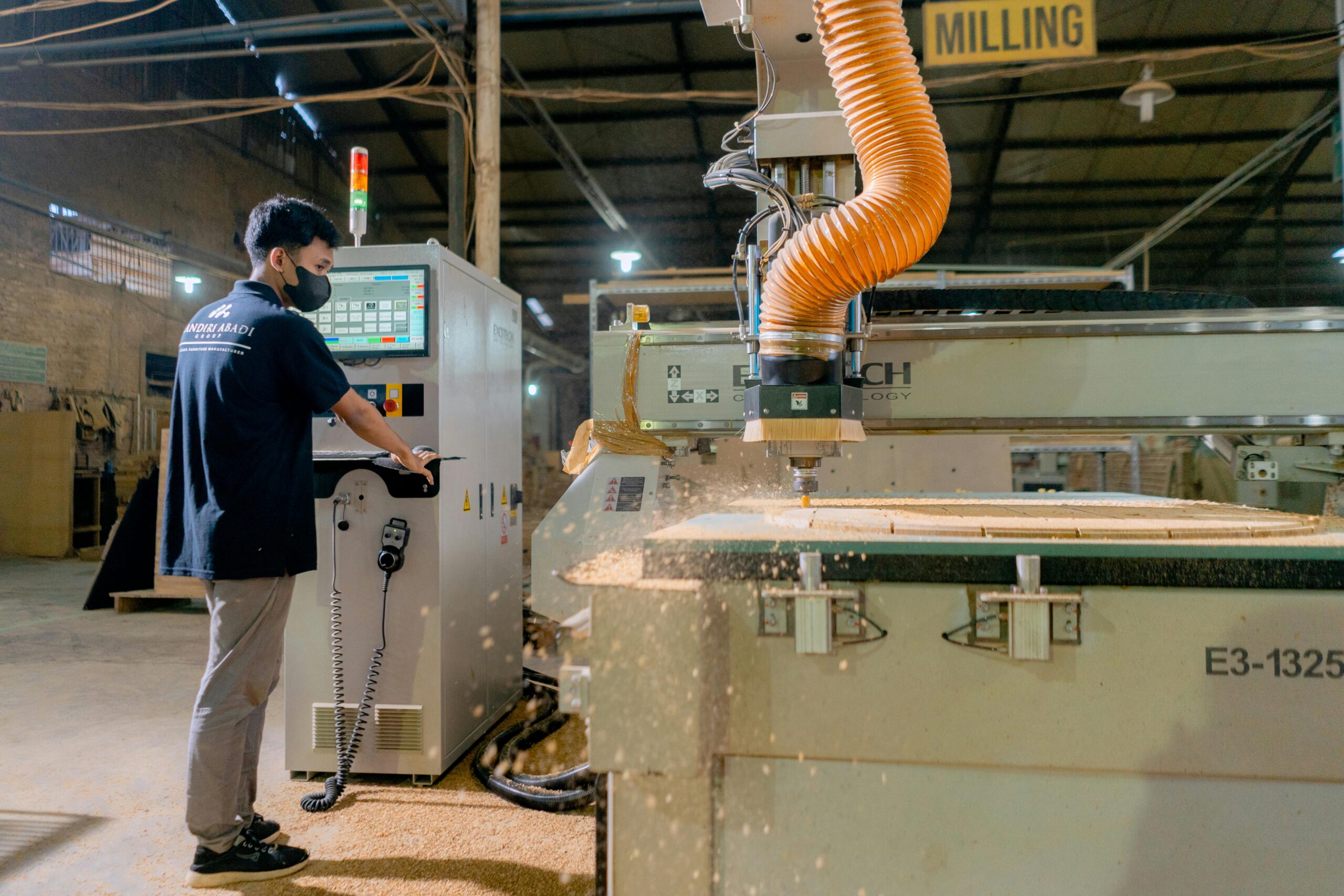 An industrial worker oversees a milling machine in a busy factory environment.